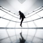 A person seemingly levitates in a contemporary room with reflections and shadows.