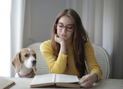 pexels-photo-3786748-3786748 Young woman reading a book with her dog beside her indoors.